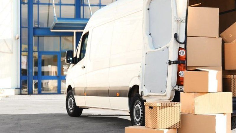 Furgoneta de mudanzas con las puertas abiertas y cajas apiladas junto a ella