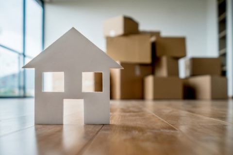 Maqueta de una casa sobre el parquet con cajas de mudanza apiladas al fondo