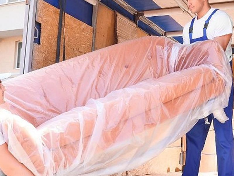 Dos operarios de mudanzas cargando un sofá embalado en film dentro del camión